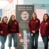 Picture showing four women standing beside of a NSTEM poster
